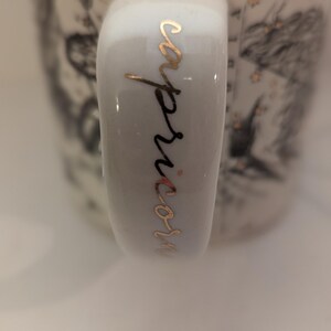 May include: White ceramic mug with a gold inscription that reads "capricorn" on the handle.