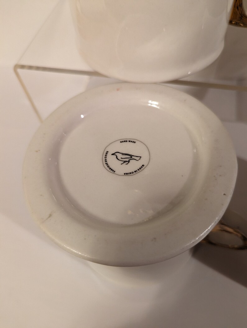 Pu&ograve; includere: Tazza in ceramica bianca con un design di uccello nero e il testo "Hand Wash" e "Made in China" sul fondo.