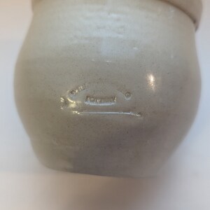 May include: A white ceramic crock with a round body and a wide opening. The crock has a stamped inscription that reads "Smith Pottery Co.  Fort Worth".
