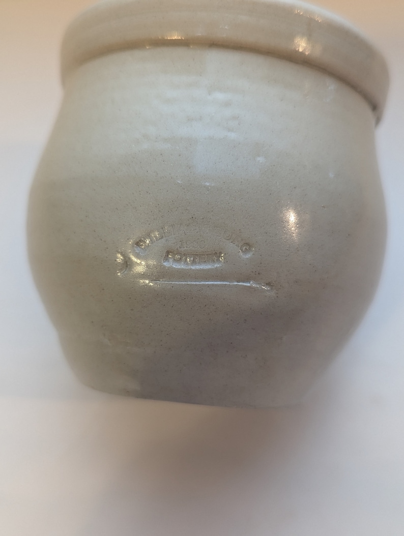 May include: A white ceramic crock with a round body and a wide opening. The crock has a stamped inscription that reads "Smith Pottery Co.  Fort Worth".