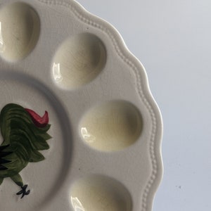 Puede incluir: Plato de huevos de cer&aacute;mica blanca con seis hendiduras individuales para huevos. El plato presenta un dise&ntilde;o de gallo verde y rojo.