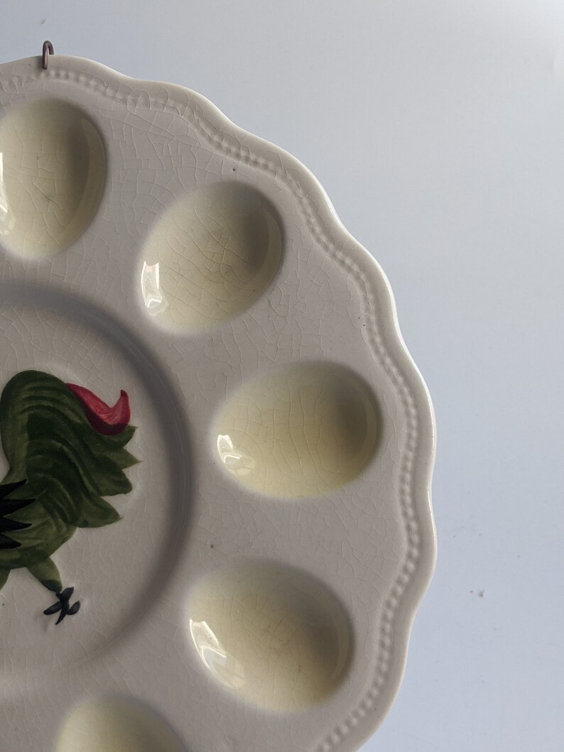Puede incluir: Plato de huevos de cer&aacute;mica blanca con seis hendiduras individuales para huevos. El plato presenta un dise&ntilde;o de gallo verde y rojo.