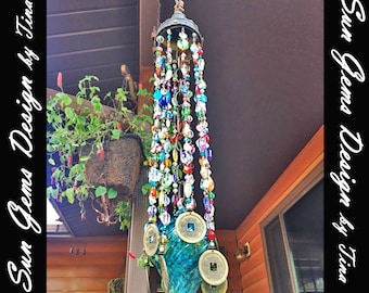 May include: A colorful wind chime with a decorative metal top and strands of beads in various colors. The wind chime features a turquoise glass base and several gold-colored coins. The text "Sun Gems Design by Tina" is visible.