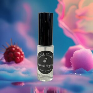 May include: A clear glass perfume bottle with a black cap. The label reads "Dabble Scents Pastel Skyline Extract de Parfum". The background is a blurred mix of pink, blue, and purple hues, with a raspberry and a pink cloud-like shape.
