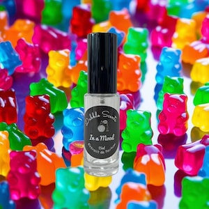 May include: A clear glass bottle with a black cap and label. The label says "Dabble Scents" and "In a Mood" with a small image of a gummy bear. The bottle is surrounded by colorful gummy bears.