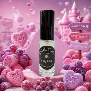 May include: A clear glass perfume roller bottle with a black cap and a circular label reading Dabble Scents Candy Hearts Extrait de Parfum. The bottle is surrounded by purple grapes and pink heart-shaped candies labeled Sweet Tarts.