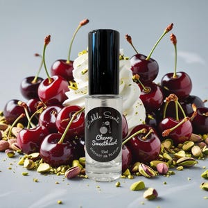 May include: A clear perfume bottle with a black cap, labeled "Cherry Sweetheart," sits amidst fresh cherries, whipped cream, and pistachios. The bottle contains 15ml of perfume. The cherries are a deep red color.