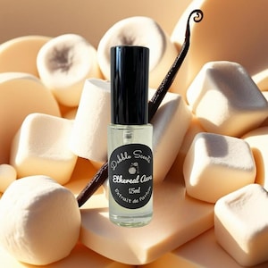 May include: A small glass bottle of perfume with a black cap and label. The label reads "Dabble Scents Ethereal Aura 15ml Extrait de Parfum". The bottle is surrounded by white marshmallows and a vanilla bean.