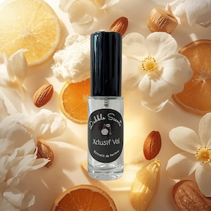 May include: A clear perfume bottle with a black cap, labeled "Dabble Scents Xclusif Val Extrait de Parfum." The bottle is surrounded by white flowers, orange slices, and almonds, creating a natural, fresh aesthetic.