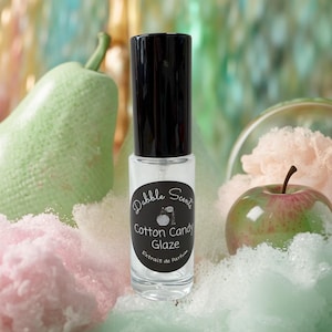 May include: A clear glass perfume bottle with a black cap and a circular label. The label features the text Dabble Scents, Cotton Candy Glaze, and Extrait de Parfum, along with a small illustration of a vintage perfume atomizer bottle.