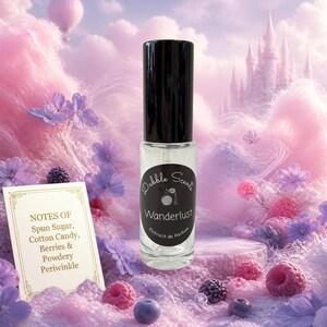May include: A clear glass perfume roller bottle with a black cap and a black oval label reading Dabble Scents Wanderlust Extrait de Parfum. A white card lists notes of Spun Sugar, Cotton Candy, Berries, and Powdery Periwinkle in gold text.