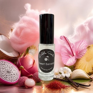 May include: A clear glass perfume bottle with a black cap and a black circular label featuring the text Dabble Scents Sweet Baccarat Extrait de Parfum. The bottle is surrounded by pink cotton candy, dragon fruit, lychee, pineapple, and saffron.