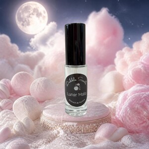 May include: A clear glass perfume roller bottle with a black cap and a black circular label. The label features white text that reads Dabble Scents, Lunar Mallo, and Extrait de Parfum, along with a small graphic of a perfume atomizer bottle.
