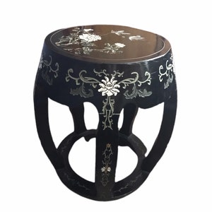 May include: Black, round, decorative stool with floral and bird inlay. The stool features a dark finish with intricate mother-of-pearl designs. The legs are curved and connected by a lower ring.