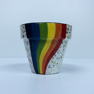 May include: A white ceramic planter with a rainbow design and a speckled white glaze.