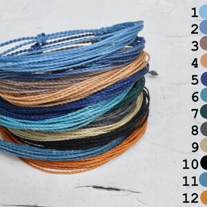 Puede incluir: Un conjunto de 12 pulseras coloridas hechas de cuerda trenzada. Las pulseras son de varios tonos de azul, turquesa, verde, marrón, naranja, negro y gris.