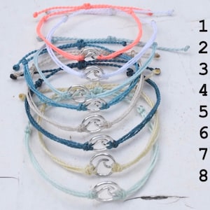 Puede incluir: Ocho pulseras de amistad coloridas con un dije de ola plateado. Las pulseras son en tonos de coral, azul claro, azul, beige, azul verdoso, crema y verde claro.