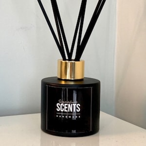 May include: Black glass diffuser bottle with a gold collar, holding black reeds. The bottle has a label that reads "Signature SCENTS HANDMADE". A home fragrance product.