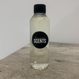 May include: A clear, cylindrical bottle with a black cap. The bottle contains a clear liquid and has a black circular label with the words "Signature SCENTS" in white. The bottle is on a grey, textured surface.
