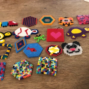 May include: A collection of colorful, handmade bead art, including a turtle, a fish, a heart, a panda, and a variety of geometric shapes.