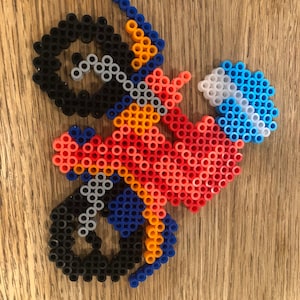 May include: A red, orange, blue, black, and white bead mosaic of a dirt bike with a rider wearing a helmet.