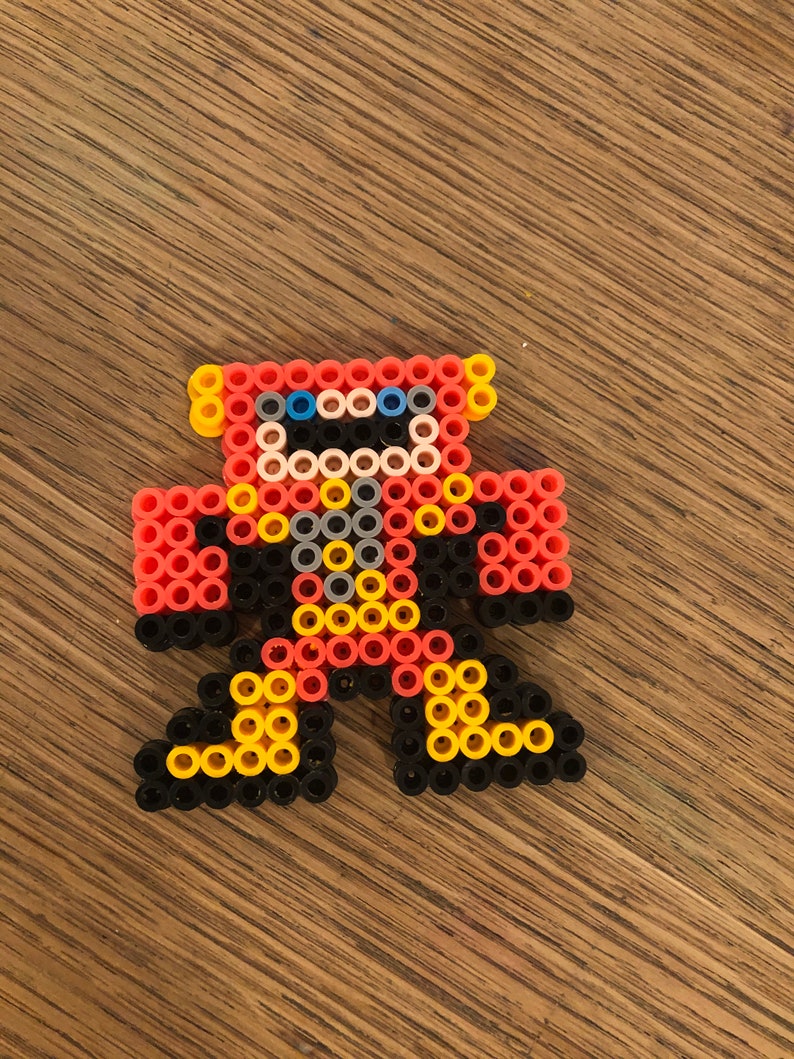 May include: A red, yellow, black, and blue robot made of small plastic beads. The robot has a round head, two arms, and two legs.