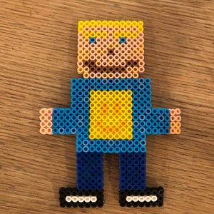 May include: A blue and yellow pixel art figure of a person with blonde hair, wearing a blue shirt with a yellow square on the front, blue pants, and black shoes.