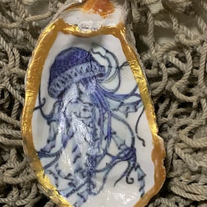 May include: A white oyster shell with a gold rim, painted with a blue and white jellyfish design.