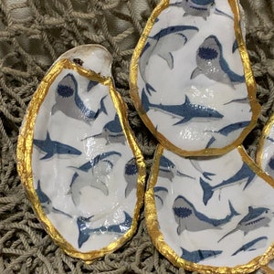 May include: Three oyster shells with gold trim, each painted with a white background and a pattern of blue sharks.