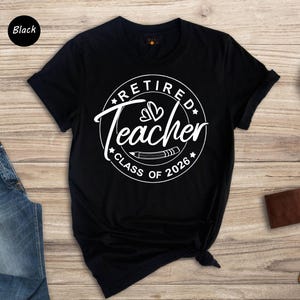 a black t-shirt with a white graphic design, a pair of blue jeans, a brown wallet, a watch, and a small potted plant on a wooden surface.