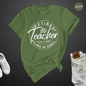 a green t-shirt with a white graphic design, a pair of white sneakers, and a pair of white jeans, all laid out on a dark background.