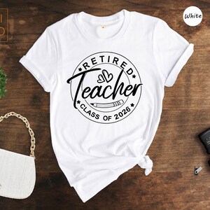 a white t-shirt with a graphic design, a white purse, a camera, and a plant on a wooden surface.