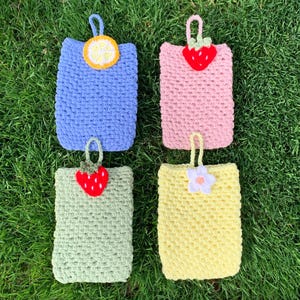 May include: Four rectangular crochet pouches with hanging loops. The top left is blue with a yellow lemon slice, the top right is pink with a red strawberry, the bottom left is light green with a red strawberry, and the bottom right is yellow with a white flower.