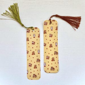 Op de afbeelding: Twee rechthoekige bladwijzers met een lichtgele achtergrond met een herhalend patroon van kleine bruine eekhoorns, uilen en herfstbladeren. De linker bladwijzer heeft een groene kwast en de rechter bladwijzer heeft een bruine kwast.
