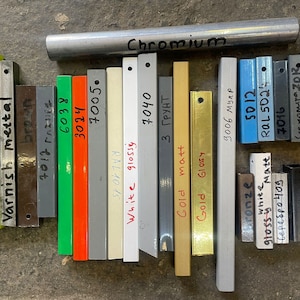 May include: A collection of metal samples in various finishes, including varnish, metal, brown, green, orange, grey, white, gold, and chrome. The samples are labelled with their respective finishes and colours.
