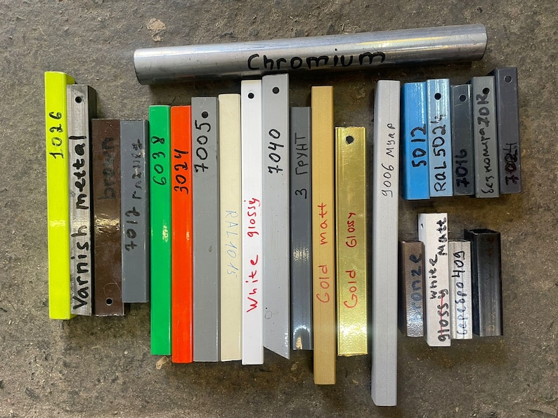 May include: A collection of metal samples in various finishes, including varnish, metal, brown, green, orange, grey, white, gold, and chrome. The samples are labelled with their respective finishes and colours.