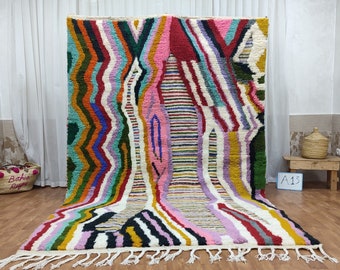 Puede incluir: Una alfombra marroquí colorida con un patrón geométrico en tonos de rosa, verde, amarillo, naranja y azul. La alfombra tiene un fondo blanco y flecos blancos.