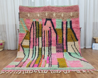 May include: A colorful Moroccan rug with geometric patterns in shades of pink, green, brown, and black. The rug has a fringe border.