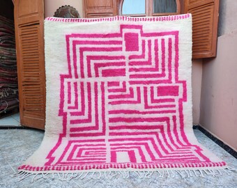May include: A white and pink geometric patterned rug with a fringe border. The rug has a modern design with pink lines and squares on a white background.