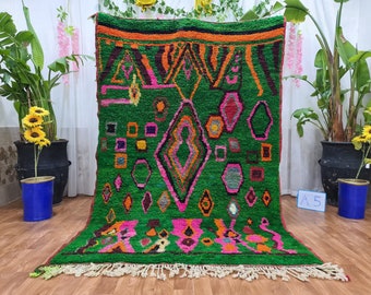 Può includere: Un vivace tappeto verde con motivi geometrici rosa, arancioni e neri. Il tappeto presenta forme a diamante, esagono e quadrato, con una frangia lungo il bordo inferiore. Il design è audace e colorato, adatto per aggiungere un elemento di spicco a qualsiasi stanza.
