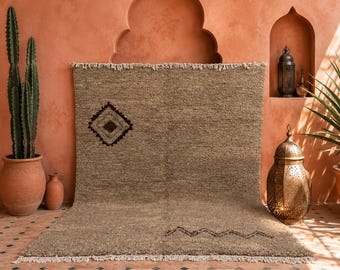 May include: A beige rug with a geometric diamond pattern and a zigzag design. The rug has a fringed edge and is displayed against a terracotta-colored wall. A potted cactus and decorative lanterns are also in the image.