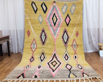 May include: A yellow, pink and grey Moroccan rug with a diamond pattern. The rug has a fringe border.