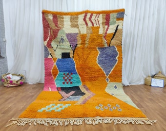 May include: A colourful Moroccan rug with a geometric pattern in shades of orange, blue, pink, and green. The rug has a fringe border and is made of wool.