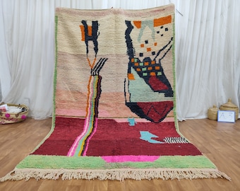 May include: A colorful Moroccan rug with abstract geometric designs in shades of pink, green, blue, black, and white. The rug has a fringe border.