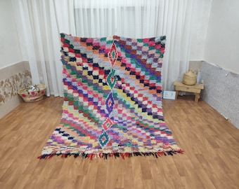 May include: A colorful Moroccan rug with a geometric pattern in shades of pink, blue, green, yellow, and red. The rug has a fringe border and is made of wool.