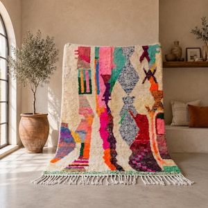 Può includere: Un tappeto rettangolare con base color crema caratterizzato da un vivace motivo astratto multicolore. Il design include forme geometriche, strisce verticali e motivi a rombi in tonalità rosa acceso, verde acqua, arancione, viola e rosso, rifinito con frange bianche.