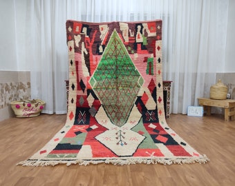 May include: A large, colorful Moroccan rug with geometric patterns in shades of red, green, black, and white. The rug has a fringe border and is laid out on a wooden floor.