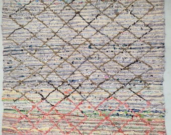 May include: A handmade rug with a diamond pattern. The rug features a neutral color palette with a mix of light gray, beige, and colorful accents. The diamond pattern is created with brown and red lines.