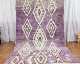 May include: A purple and white Moroccan rug with a diamond pattern. The rug has a fringe border and is made of wool.