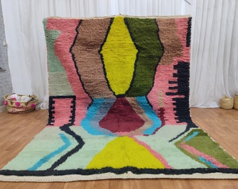 Könnte beinhalten: Ein bunter abstrakter Teppich mit geometrischen Formen in den Farben Rosa, Grün, Gelb, Blau und Braun. Der Teppich hat einen weißen Rand und ist aus Wolle gefertigt.